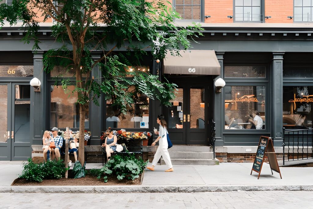 alt="People relaxing in a cozy café with large windows overlooking a lively New York city street"