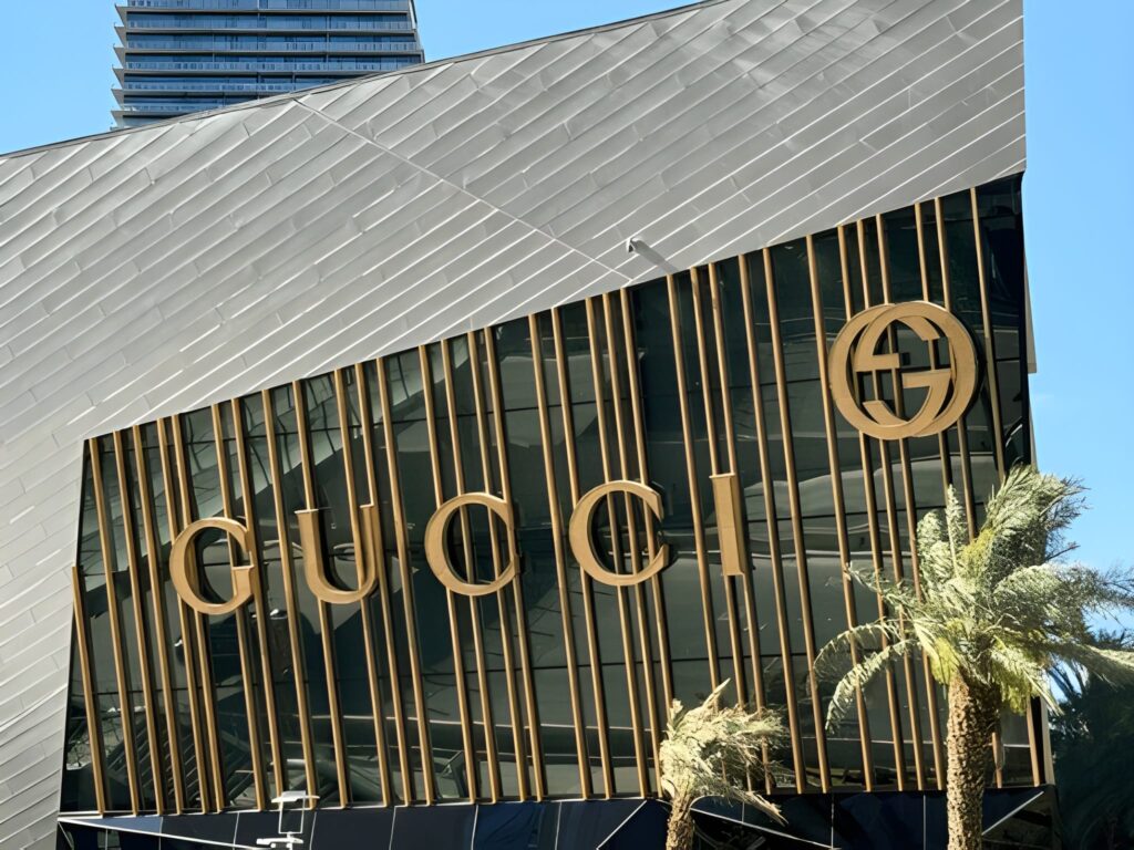 alt="Gucci mural and colorful street art on a city wall with people taking photos"